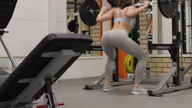 Spor salonunda halterle çömelmiş zinde bir kadın.