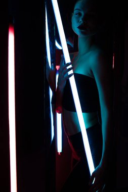 Parlak lamba ile tüm vücudu şehvetli kadın karanlık odada duvara yaslanmış neon ışıklı.