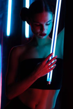 Parlak lamba ile tüm vücudu şehvetli kadın karanlık odada duvara yaslanmış neon ışıklı.