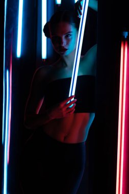 Parlak lamba ile tüm vücudu şehvetli kadın karanlık odada duvara yaslanmış neon ışıklı.