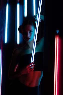 Parlak lamba ile tüm vücudu şehvetli kadın karanlık odada duvara yaslanmış neon ışıklı.