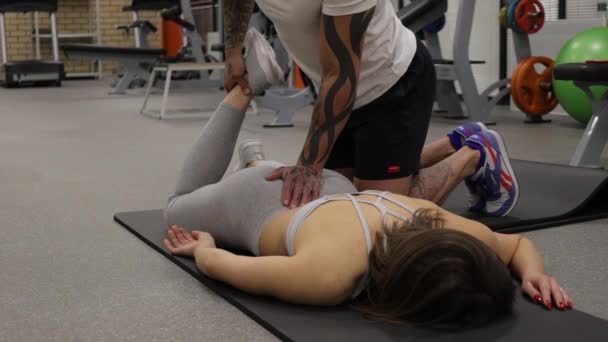 Entraîneur personnel étirant les jambes de la sportive dans la salle de gym — Video