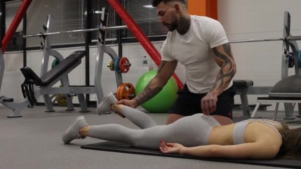 Entraîneur personnel étirant les jambes de la sportive dans la salle de gym — Video