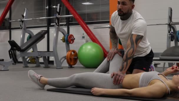 Personal Trainer streckt Beine von Sportlerin im Fitnessstudio — Stockvideo