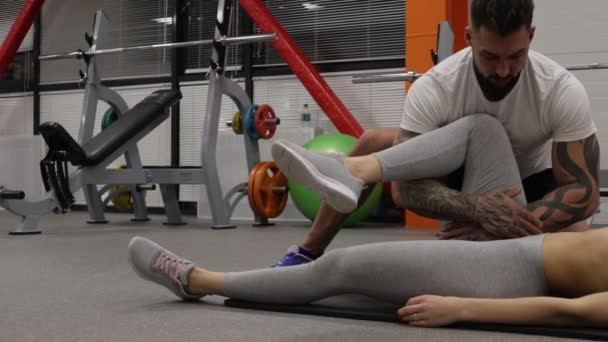 Personal trainer stretching legs of sportswoman in gym — Stock Video