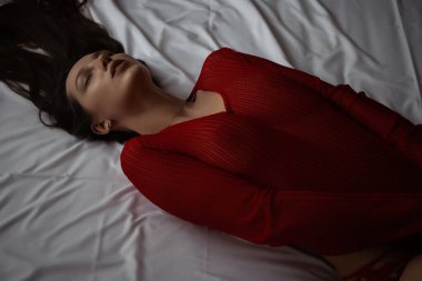 Yukarıdan, iç çamaşırlı, gözleri kapalı, yatakta uzanmış, ince, seksi bir kadın.