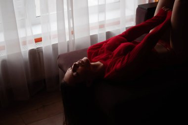 Kırmızı örgü süveter ve seksi dantel külotlu, yatakta uzanmış, şehvetli genç bir kadının yüksek açılı yan görüntüsü.