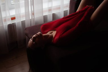 Kırmızı örgü süveter ve seksi dantel külotlu, yatakta uzanmış, şehvetli genç bir kadının yüksek açılı yan görüntüsü.