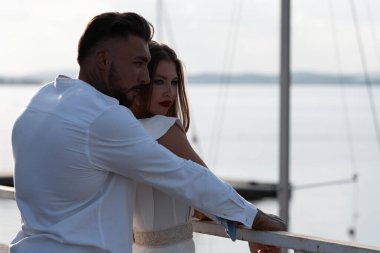 Moda kıyafetleri içinde sevgi dolu bir çift yazın teknelerle limanda beklerken kucaklaşıyorlar.