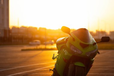 Tanımlanamayan stil sahibi, kasklı erkek motosikletçi, günbatımı gökyüzünün arka planında, park halindeki motosiklette oturuyor.