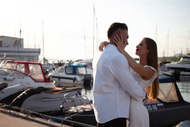 Sevgi dolu çift yazın güneşli bir günde teknelerin yanında setin kenarında dikilirken sarılıyor.