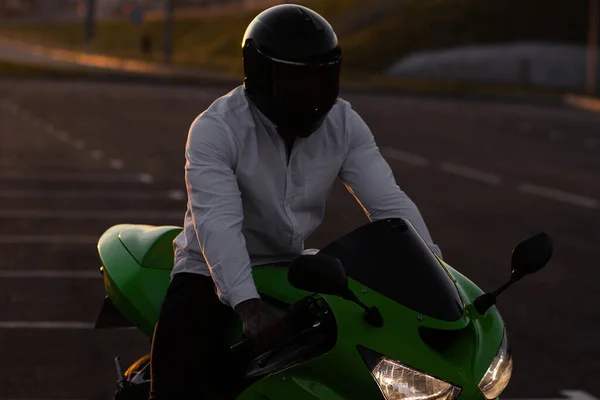 在日落的天空下 坐在城市停放的摩托车上 戴着头盔的男性摩托车手难以辨认 — 图库照片