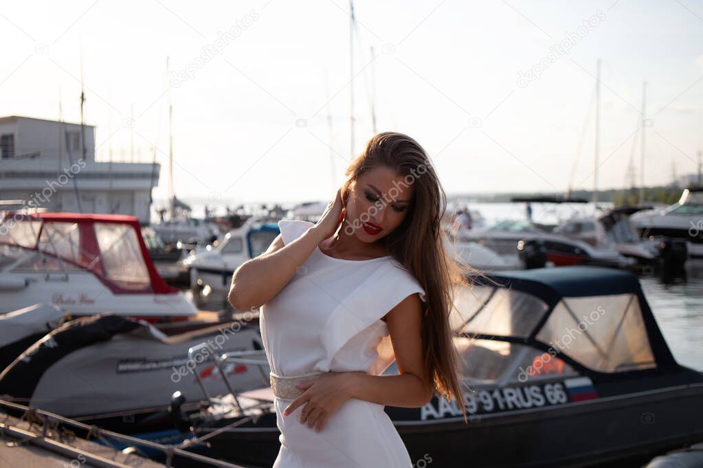 Confident female in trendy summer dress and with red lips standing near boats in harbor