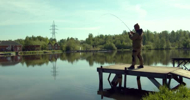 Hombre pescando en muelle de madera cerca del lago — Vídeos de Stock