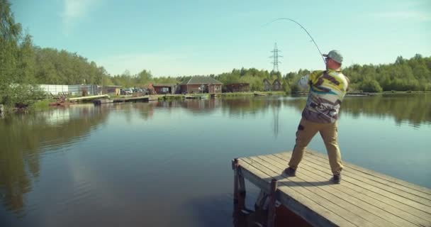 Hombre pescando en muelle de madera cerca del lago — Vídeos de Stock