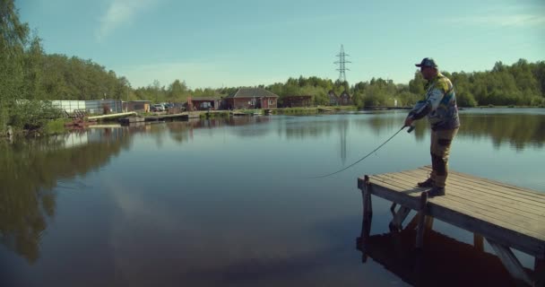 Człowiek połowów na drewnianym molo w pobliżu jeziora — Wideo stockowe