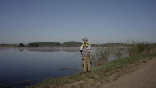 Uomo pesca sul molo di legno vicino al lago — Video Stock