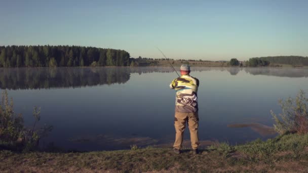 Hombre pescando en muelle de madera cerca del lago — Vídeos de Stock
