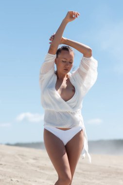 Beyaz bluzlu çekici genç kadın manken çıplak göğüs gözler kapalı ve kollar havada dururken yaz mevsiminde mavi gökyüzüne karşı özgürlük ve güneş ışığının tadını çıkarıyor.