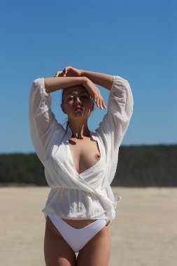 Beyaz bluzlu çekici genç kadın manken çıplak göğüs gözler kapalı ve kollar havada dururken yaz mevsiminde mavi gökyüzüne karşı özgürlük ve güneş ışığının tadını çıkarıyor.