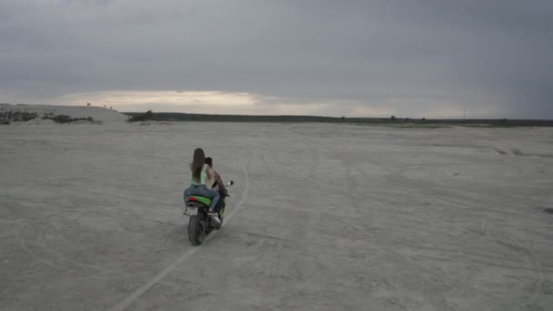 Una hermosa pareja joven hombre y mujer están montando juntos en una moto en la playa durante el atardecer — Vídeos de Stock
