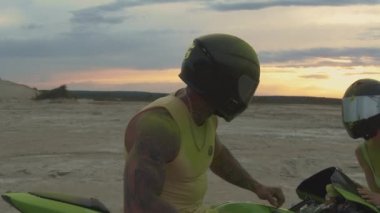 Güzel genç bir çift, gün batımında plajda motosiklet sürüyor.