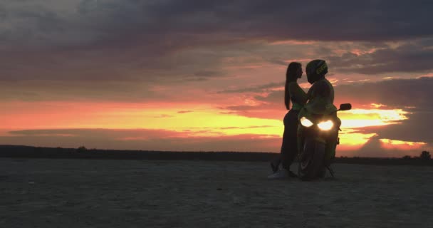 Pár objímání v blízkosti motocyklu na pláži při západu slunce — Stock video