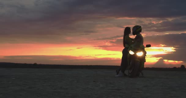 Casal abraçando perto de moto na praia ao pôr do sol — Vídeo de Stock