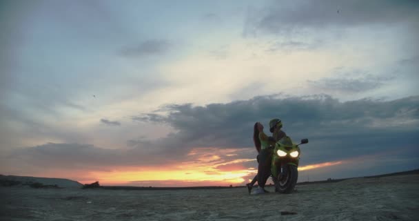 Pareja abrazando cerca de moto en la playa al atardecer — Vídeos de Stock