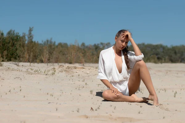 夏には砂浜に座ってファッショナブルな白い服で魅力的な若い裸足の女性の完全な体 — ストック写真