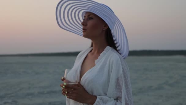 Elegante mujer con copa de vino descansando en la playa al atardecer — Vídeos de Stock