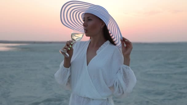 Elegante mujer con copa de vino descansando en la playa al atardecer — Vídeos de Stock