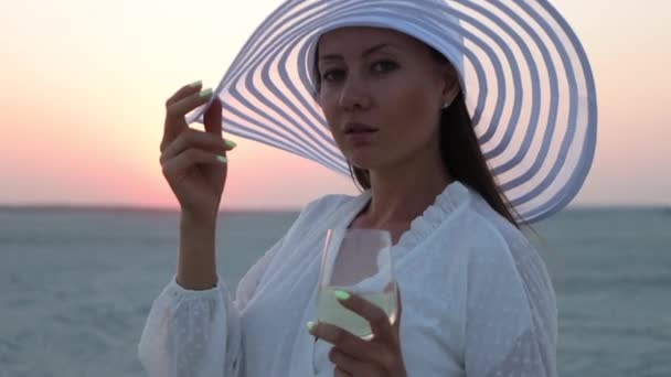 Elegante mujer con copa de vino descansando en la playa al atardecer — Vídeos de Stock