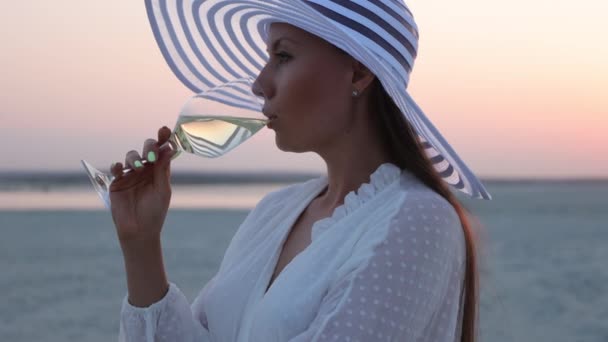 Elegancka kobieta ze szklanką wina odpoczywająca na plaży o zachodzie słońca — Wideo stockowe
