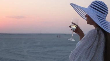 Gün batımında sahilde dinlenen bir kadeh şarapla zarif bir kadın.