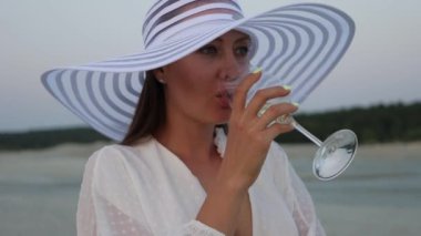 Gün batımında sahilde dinlenen bir kadeh şarapla zarif bir kadın.