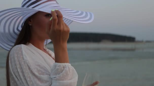 Elegancka kobieta ze szklanką wina odpoczywająca na plaży o zachodzie słońca — Wideo stockowe