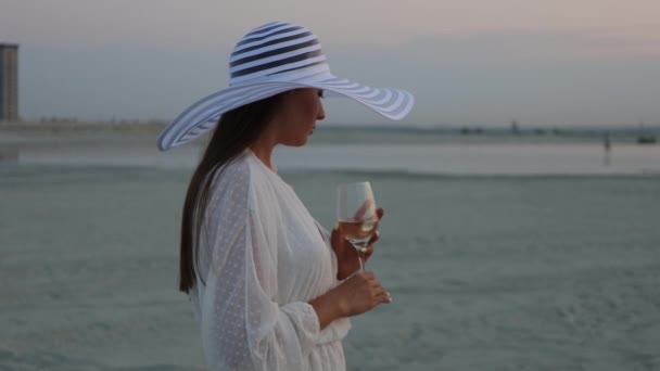 Elegante mujer con copa de vino descansando en la playa al atardecer — Vídeos de Stock