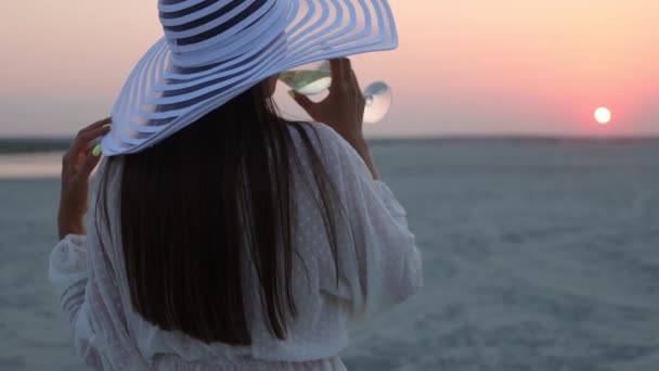 Elegant kvinna med glas vin vilar på stranden vid solnedgången — Stockvideo