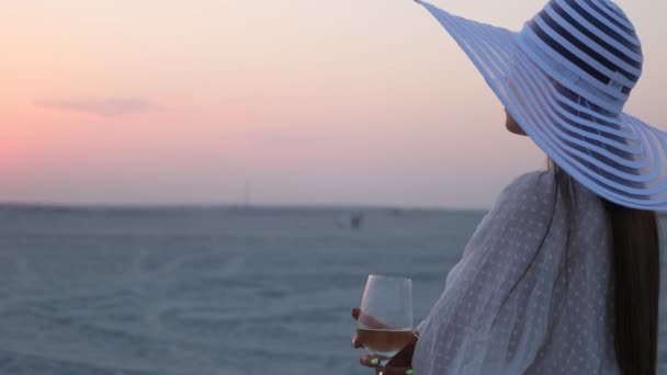 Елегантна жінка з келихом вина відпочиває на пляжі на заході сонця — стокове відео