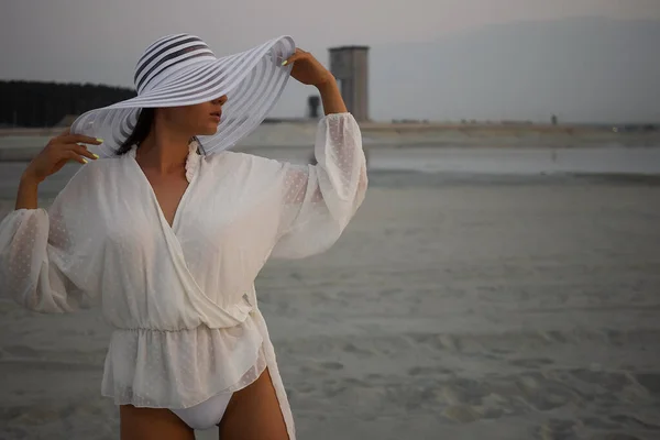 穿着超短裙和花边衬衫 头戴沙滩帽 黄昏时分站在岸上的迷人女子的侧视图 — 图库照片