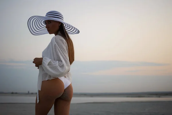 穿着超短裙和花边衬衫 头戴沙滩帽 黄昏时分站在岸上的迷人女子的侧视图 — 图库照片