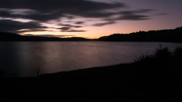 Pôr do sol filmado em exposição longa com céu nublado e fundo escuro. Tiro no lago Rotoehu localizado na região de Rotorua da Ilha do Norte da Nova Zelândia. — Fotografia de Stock