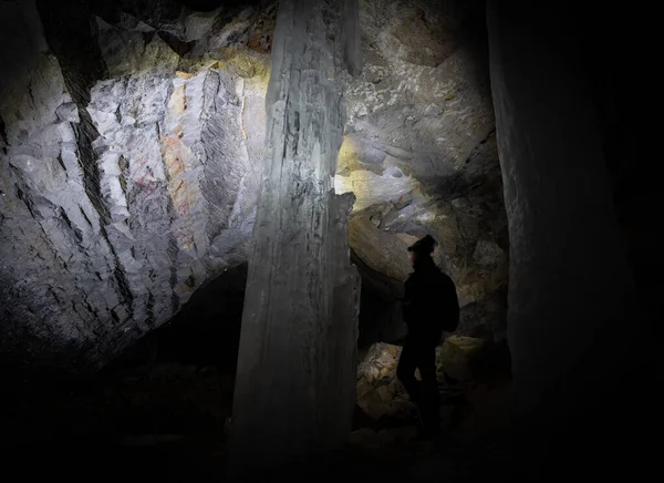 Hiker exploring dark cave illuminating it by headlamp only. Shot in Canadian Rockies on Kananaskis Ice Cave Trail, Alberta, Canada