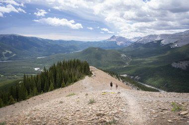 Dağ sırtlarından güzel bir vadi vadisinde, iki yürüyüşçüyle birlikte, yaz günü Kanada 'nın Nihahi Tepesi' nde çekilen patikada yürüyorlar.
