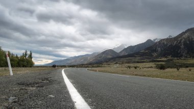 Bulutlu gökyüzü ile dağlara doğru giden yol. Yeni Zelanda 'daki Aoraki Dağı Cook Ulusal Parkı' nda düşük perspektifli çekim