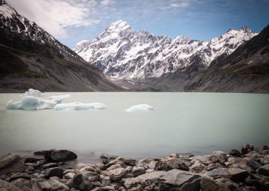 Yeni Zelanda 'daki Aoraki Cook Dağı Ulusal Parkı' nın arka planında dağ tepe noktasında yüzen buz parçalarıyla dolu buzul gölü.