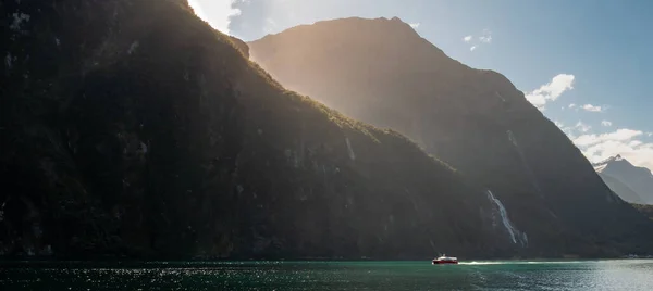 Vue panoramique du bateau naviguant à travers le fjord par une journée ensoleillée avec des rayons de soleil créant une aura dorée autour du bord des montagnes. Milford Sound, Nouvelle-Zélande — Photo