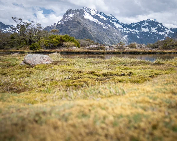 View on mountain peaks shrouded by clouds with dry grasses and small pond in foreground. Shot on Routeburn Track, New Zealand — Stock Photo, Image