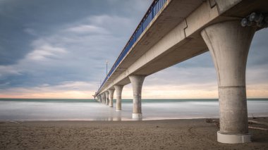 Massive concrete pier leading to horizon surrounded by ocean. Long exposure shot made in New Brighton Beach in Christchurch, New Zealand clipart